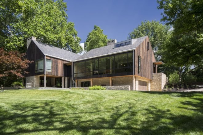 wood, stone and glass farmhouse-style home surrounded by trees