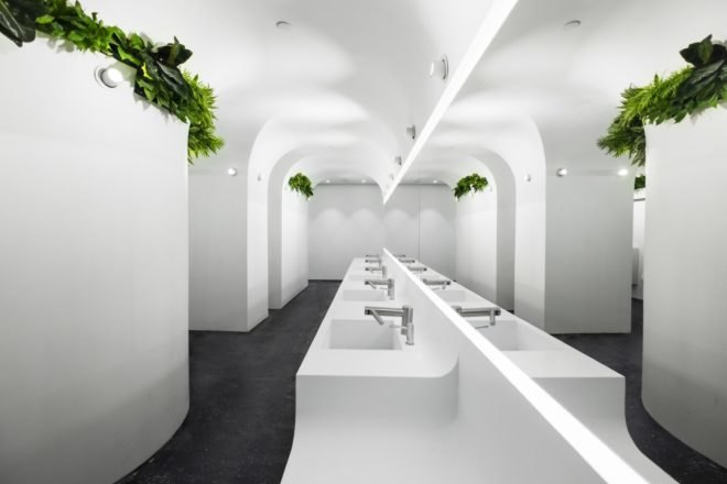 a long line of modern sinks and green plants near the ceiling