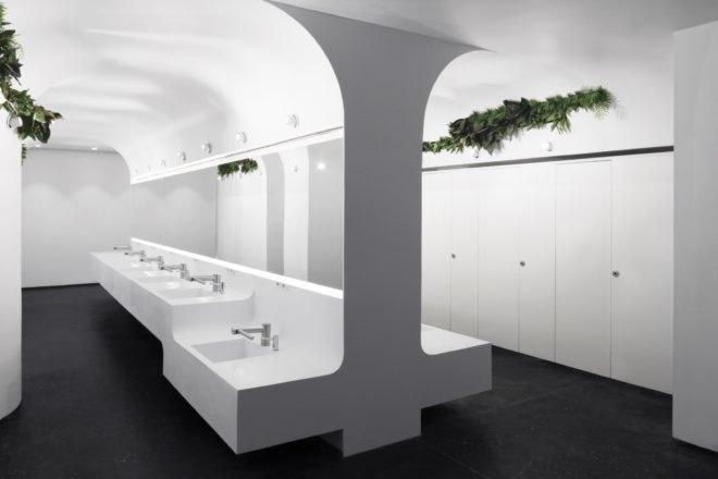 modern sinks below walls that curve into the ceiling in an all-white bathroom