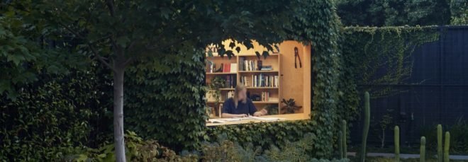 ivy-covered studio with large window revealing person working inside