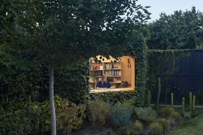 ivy-covered studio with large window revealing person working inside