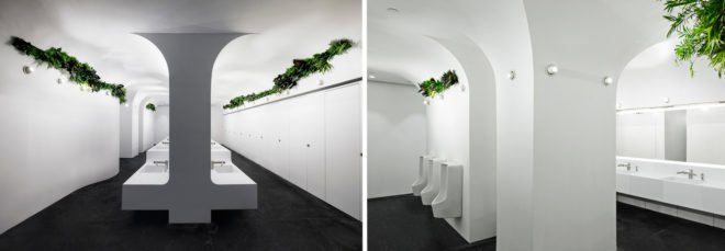 On the left, sinks in bathroom with plants near the ceiling. On the right, waterless urinals with plants above them.