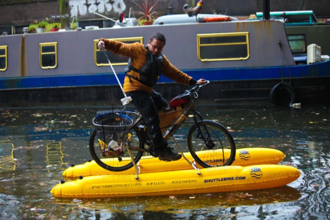 Man grabbing trash from the river while on a floating bike