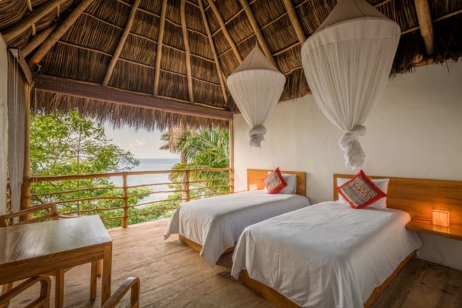 Bedroom with two beds under mosquito nets and an open wall with views of the jungle