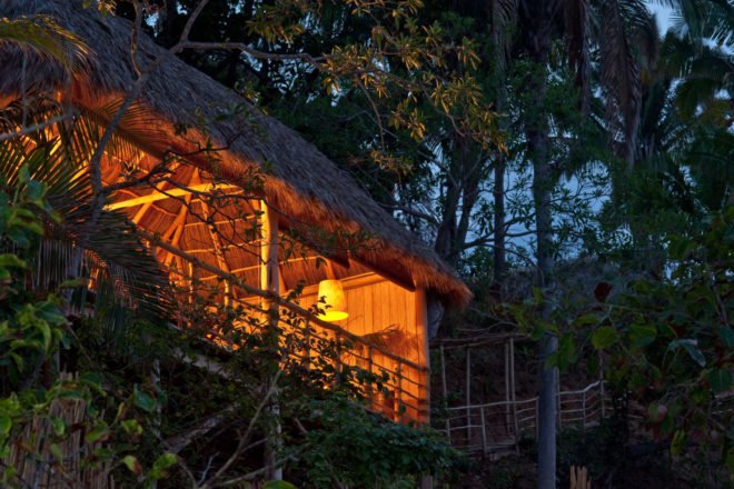 Exterior of palm-thatched cabin at night