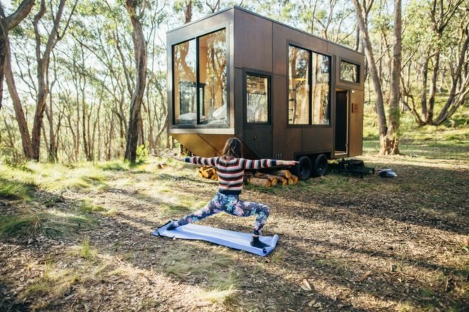 woman doing yoga in front of wooden cabin on wheels