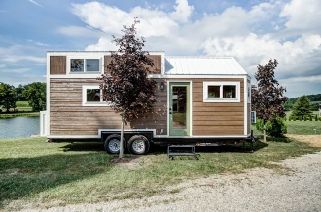 a tiny home on wheels with light wood siding and pastel green door
