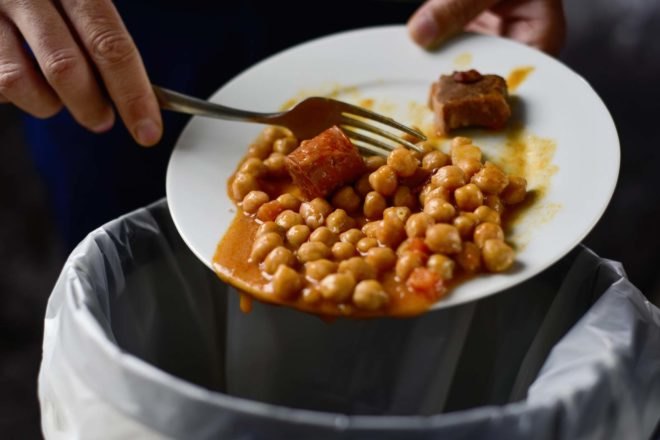 hand and fork scraping chickpeas off a plate and into the trash