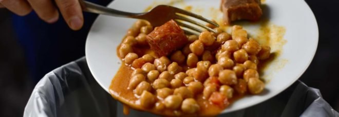 hand and fork scraping chickpeas off a plate and into the trash