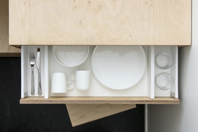 drawer opened revealing plated, bowls, mugs, glass cups and silverware