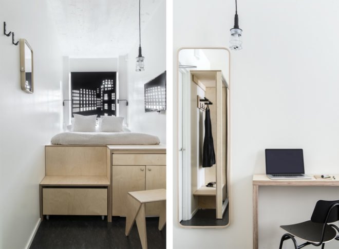 On the left, small bed on a raised light wood platform. On the right, small wood desk next to full-length mirror.