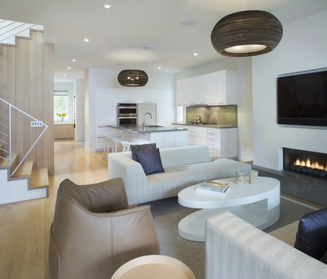 open-plan living room with white couches and leather chair and kitchen with white cabinetry