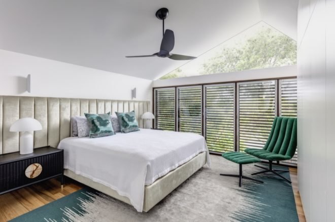 room with bed with white sheets, green pillows and slatted windows