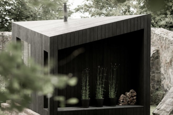 black cabin with three large plants in a narrow space