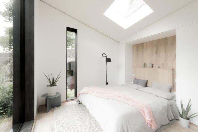 an all-white bedroom with a large bed and skylight