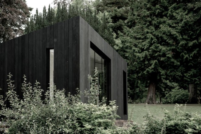 greenery in front of a black-clad cabin with large windows