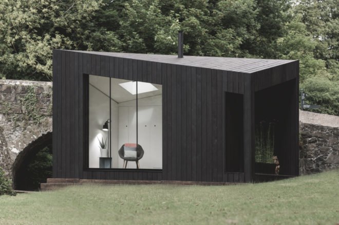black cabin with large glass window and sloped roof