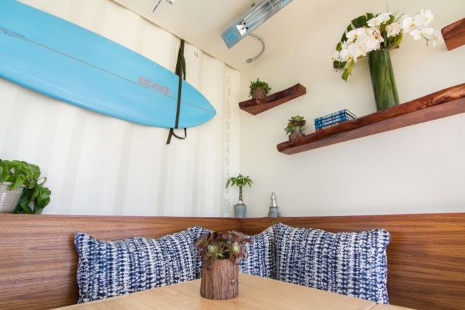 seating booth with blue and white pillows and shelves holding plants above the booth