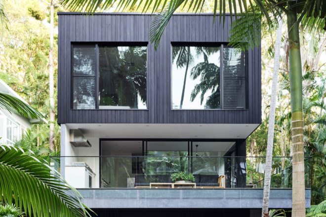 Multi-story black home with large windows surrounded by rainforest