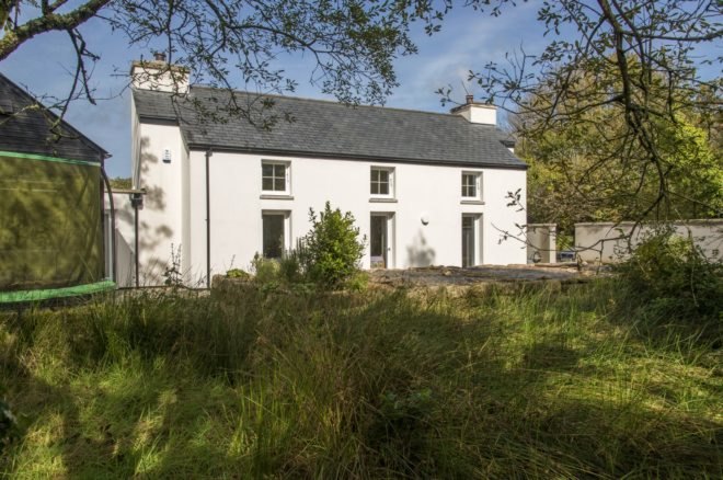 back of white cottage surrounded by greenery