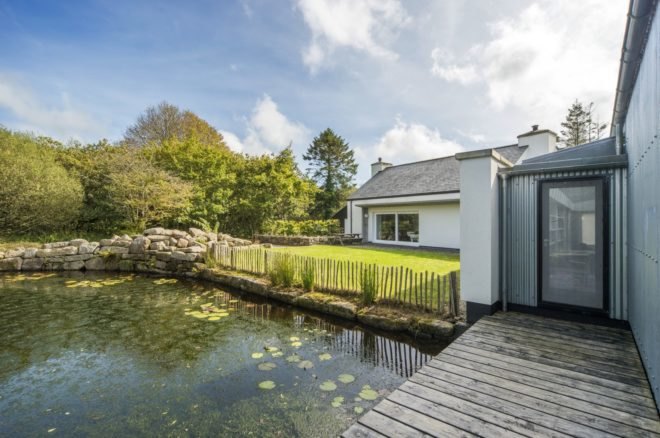 White cottage facing a pond with lily pads