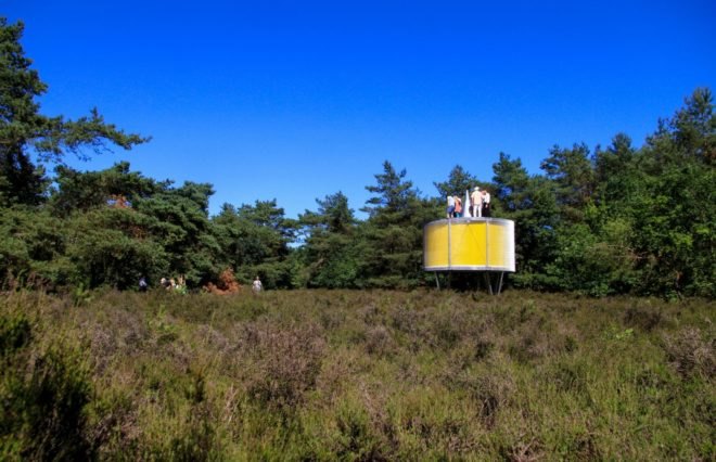round yellow pavilion on metal supports in forest landscape
