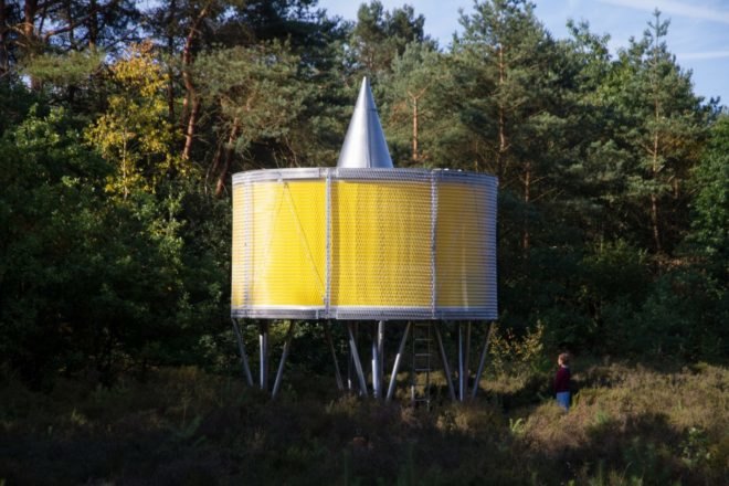 round yellow pavilion on metal supports in forest landscape