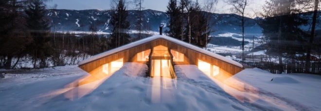 wood mountain chalet lit from within at night on a snowy landscape