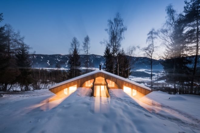 wood mountain chalet lit from within at night on a snowy landscape