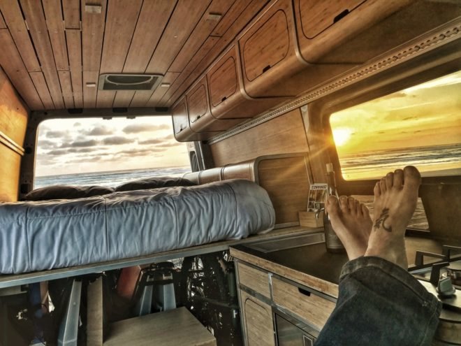 person's feet propped on cabinetry with sunset view from the windows and wine bottle on the counter