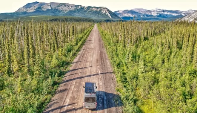 van in middle of dirt road surrounded by forest