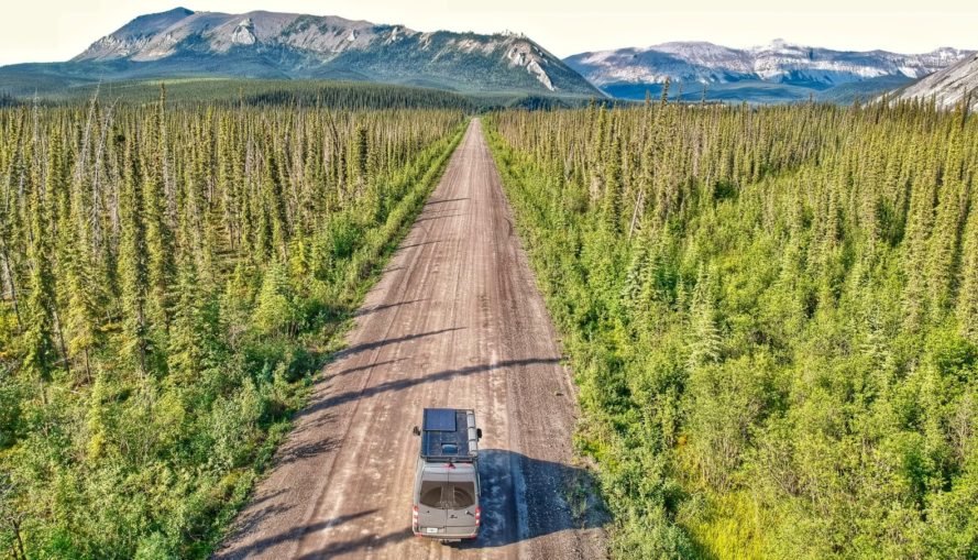 van in middle of dirt road surrounded by forest