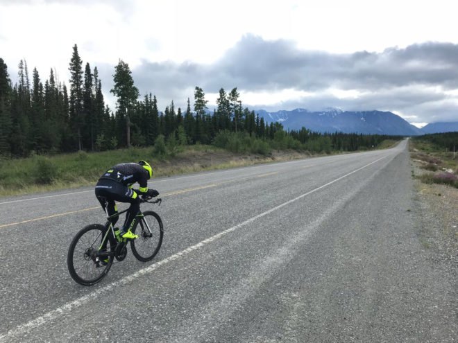 Man cycling on road with mountains in the background
