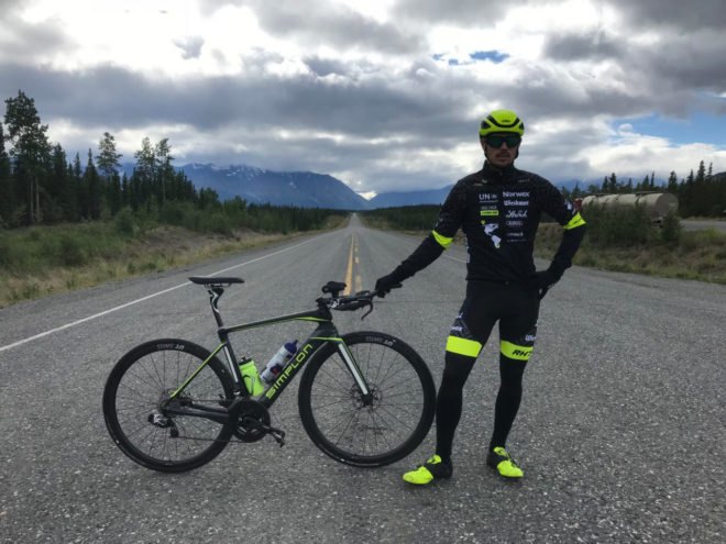 Man standing beside bike with mountains in the background