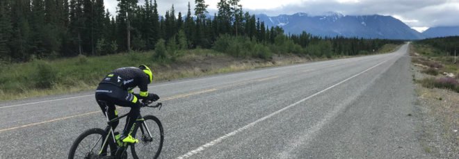Man cycling on road with mountains in the background