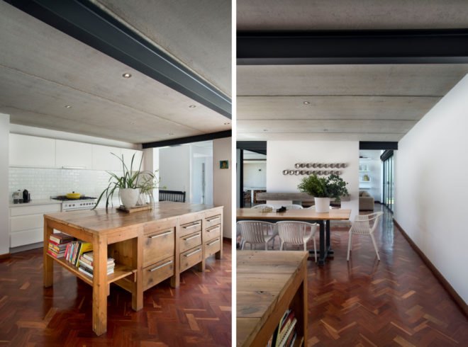 On the left, large wooden island and white cabinetry in kitchen. On the right, long wood dining table topped with large potted plant surrounded by white chairs.