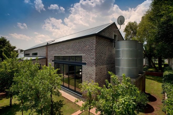 Large metal rainwater collection tanks next to brick farmhouse.