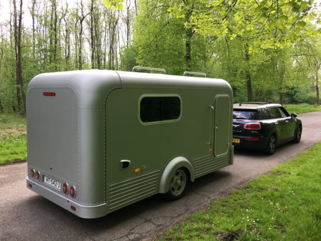 Small aluminum trailer hitched to a small car driving down a country road