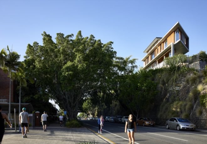 People walking on sidewalks near a cliff with timber and concrete home on top of it