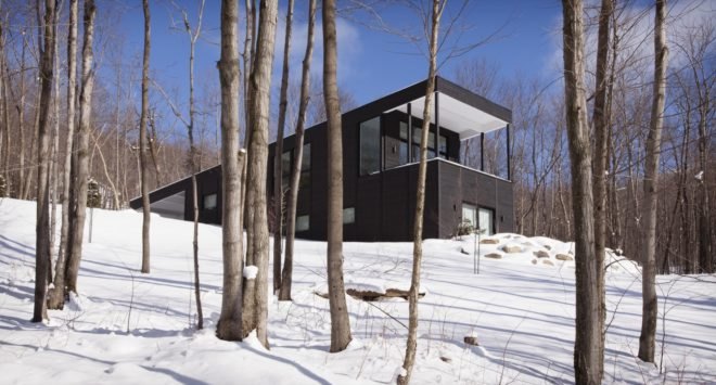 black timber home with large covered patio built into a snow-covered slope