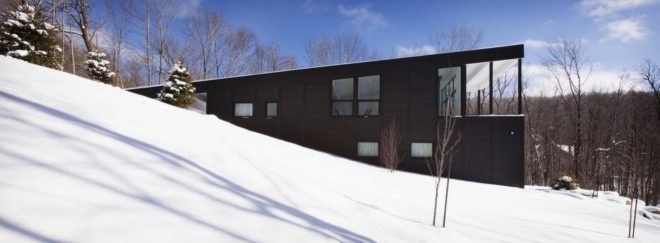 side view of black timber home built into a snowy slope