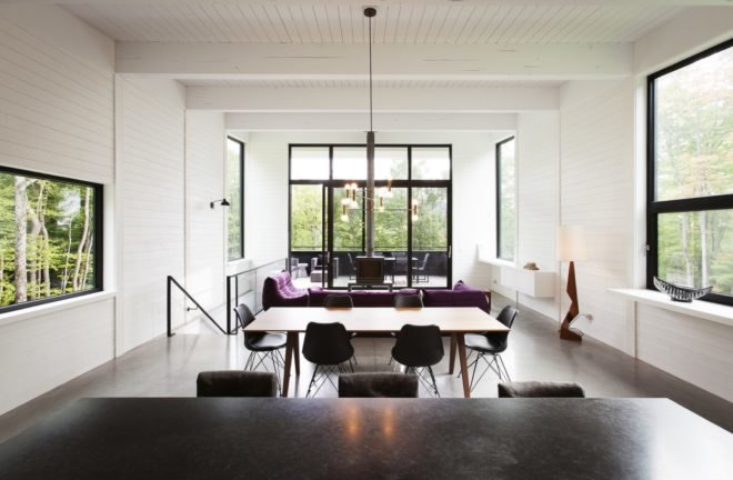 Open plan room with white walls and ceilings, a wood dining table and purple couches
