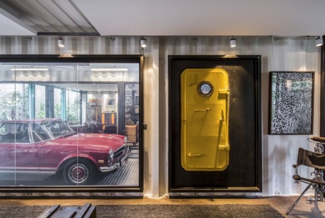 shipping container with yellow door and glass wall revealing a red vintage car