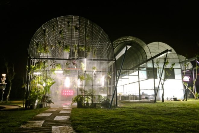 greenhouse filled with plants lit from within at night