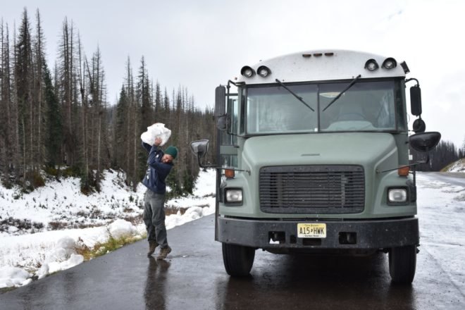 man with large chunk of snow next to green school bus