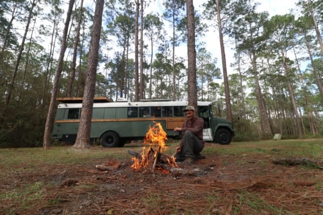 man at fire pit in front of dark green school bus