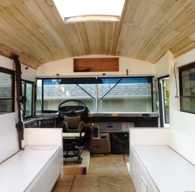 renovated school bus interior with long white benches and light wood ceilings
