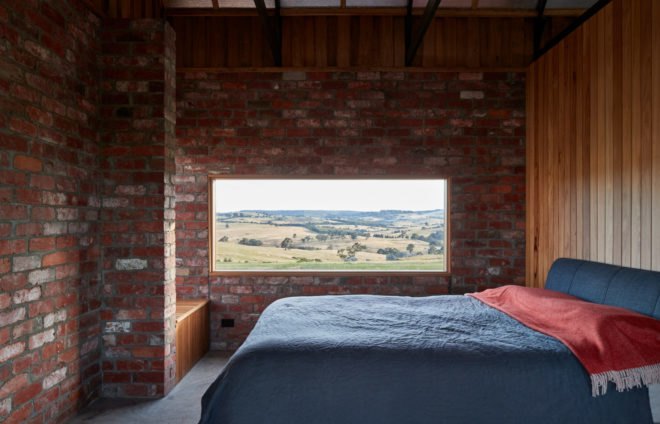 blue bed in simple room with one wood wall and other walls clad in exposed brick