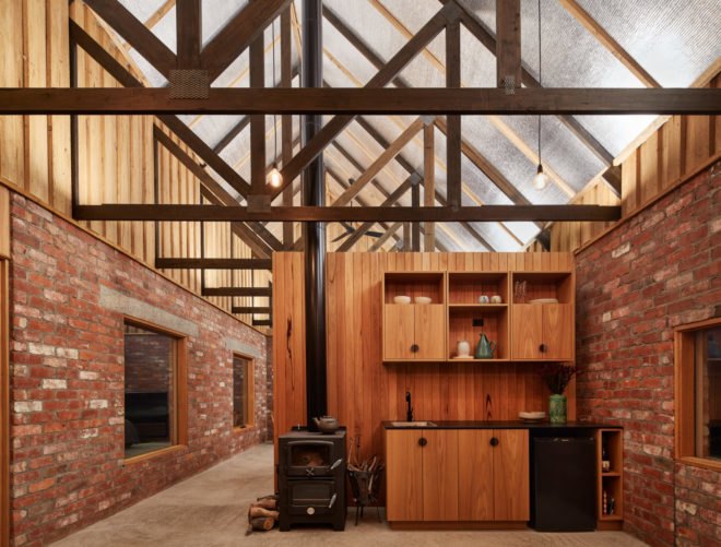 kitchen with wood cabinets and wood-burning stove in room with exposed brick walls