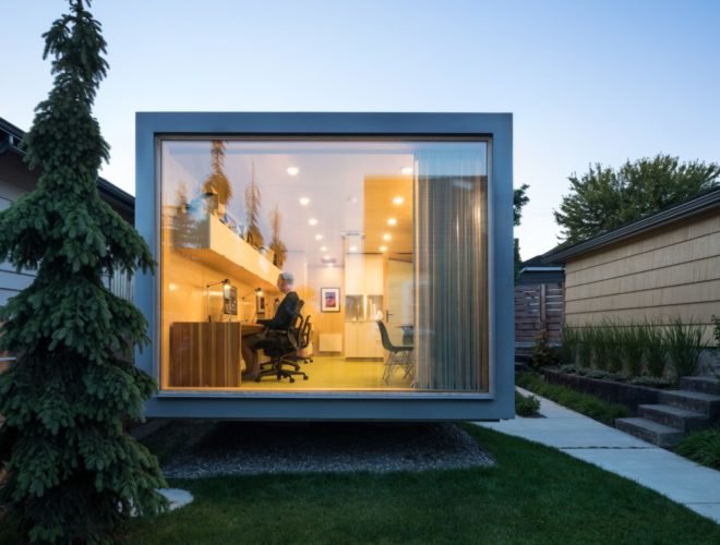 shipping container with large end window revealing man working at a desk inside